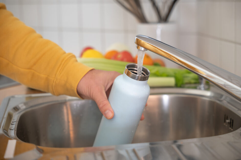 man fills up water bottle in sink