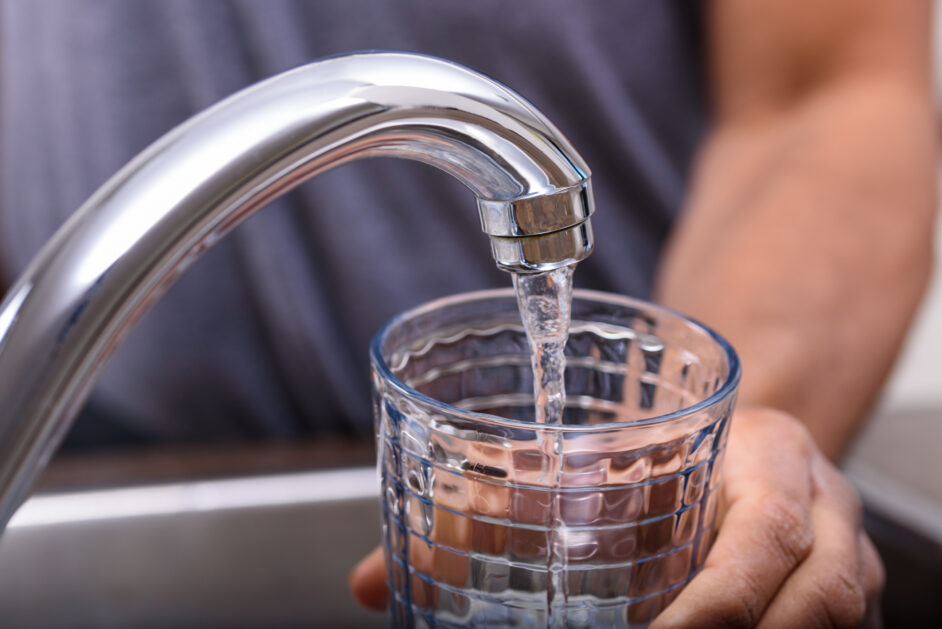 hand with drinking glass filling water from kitchen faucet