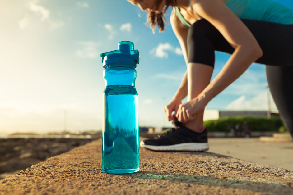 female runner tying her shoes next to bottle of water